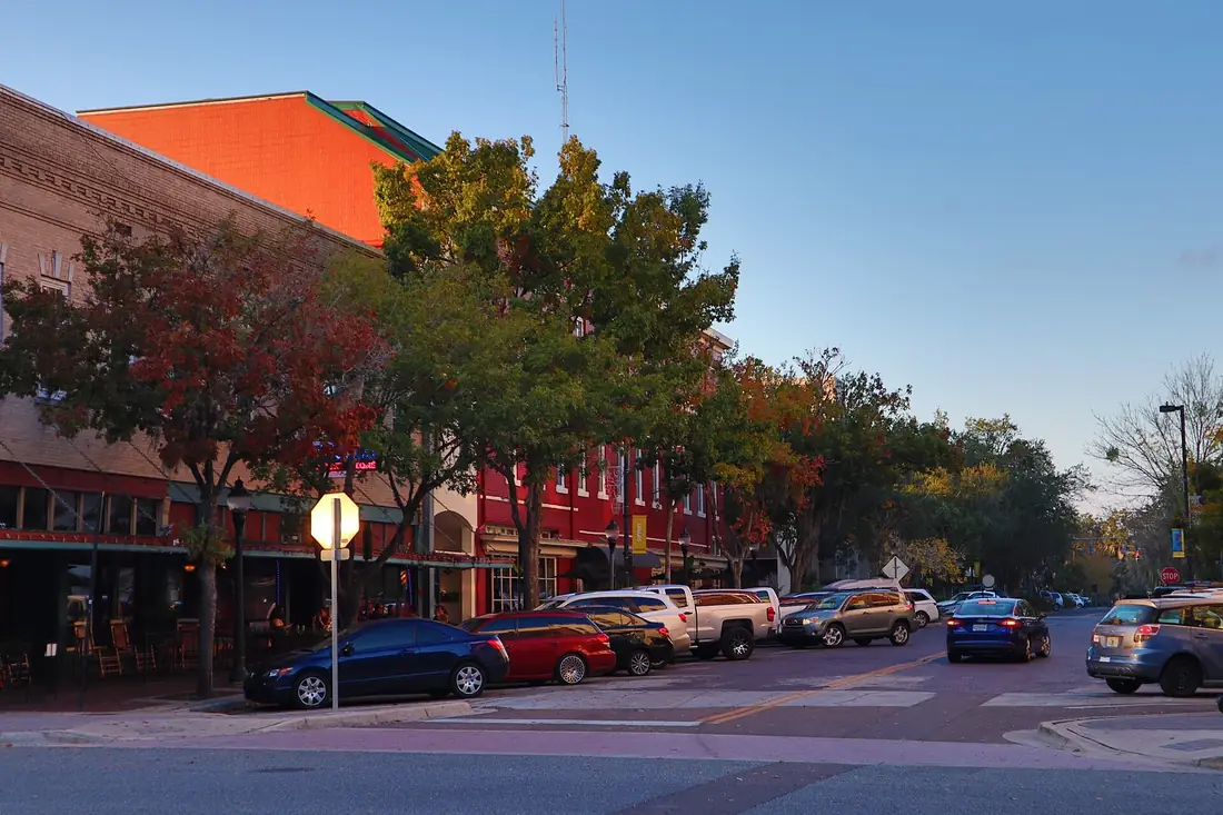 Downtown Gainesville at dusk: red brick shops, trees and parked cars along the street.